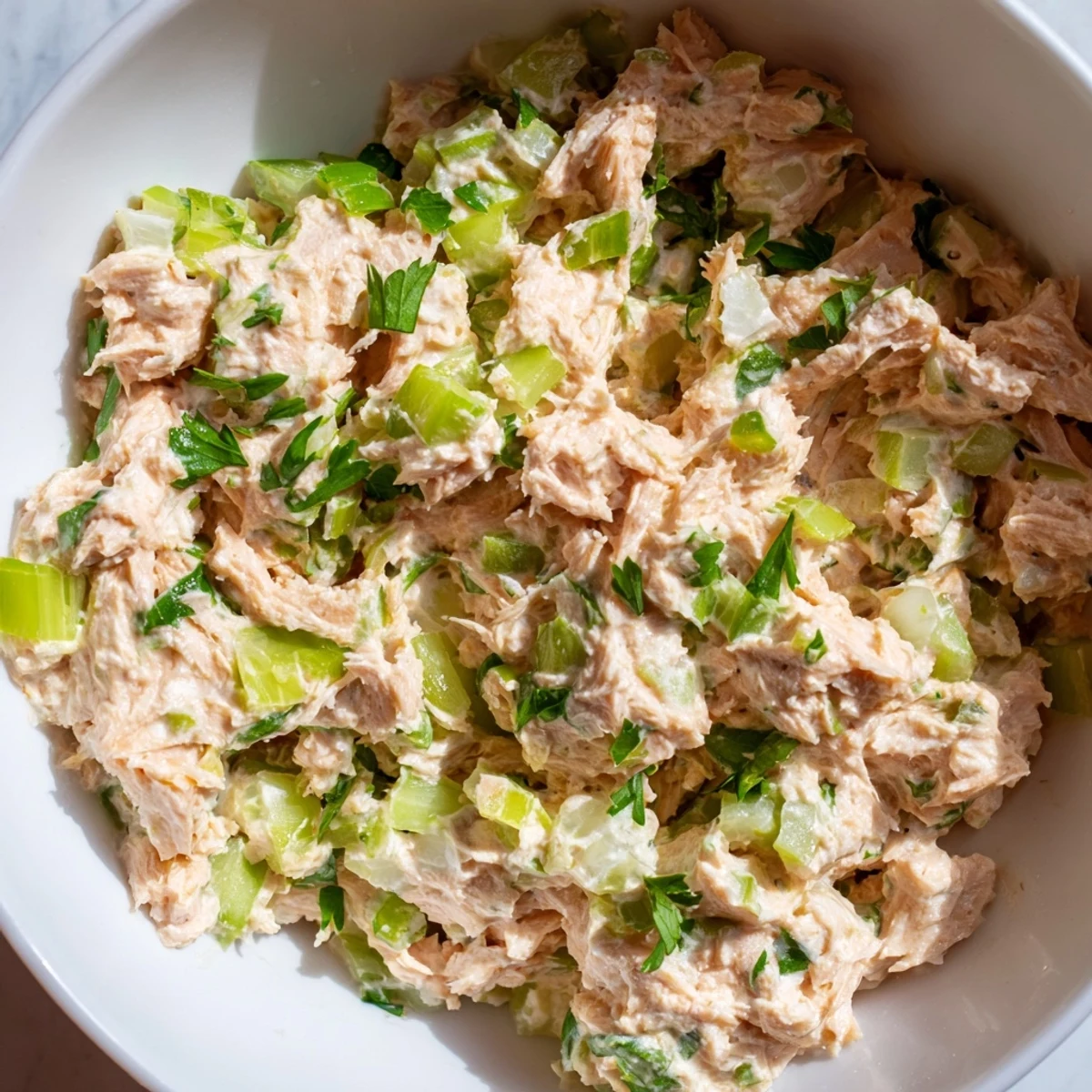 A vibrant bowl of Spicy Zesty Tuna Salad with creamy dressing, fresh scallions, and lemon wedges on the side.