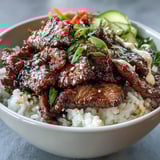 Overhead view of a Korean Beef Power Bowl with colorful toppings, sesame seeds, and green onions on steamed rice for a balanced, protein-packed meal.