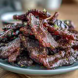 Slices of Black Currant Smoky Jerky glisten with tangy BBQ glaze, offering a rustic, sweet-and-savory snack perfect for road trips.