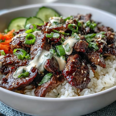 Close-up of the Korean Beef Power Bowl featuring tender marinated beef, fluffy rice, vibrant pickled carrots, crisp cucumbers, and spicy jalapeños drizzled with creamy sriracha mayo.