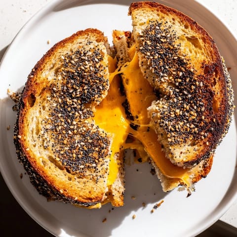 Close-up of golden brown everything bagel grilled cheese oozing melted cheddar, delicious and ready to eat.