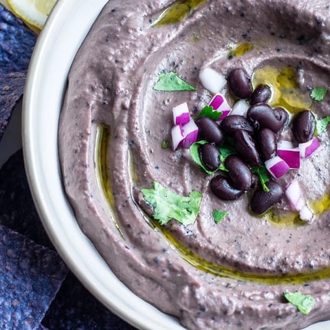 A bowl of creamy Spicy Black Bean Dip garnished with fresh cilantro, lime wedges, and sliced jalapeños for a zesty kick.
