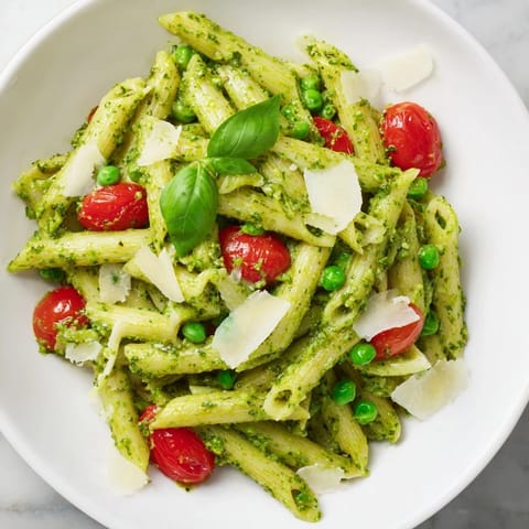 A close-up of vibrant Green Pesto Pasta Salad, tossed with olive oil and topped with halved cherry tomatoes.  