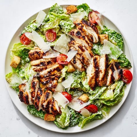A close-up view of tender grilled chicken piled atop a vibrant salad with cherry tomatoes and croutons.