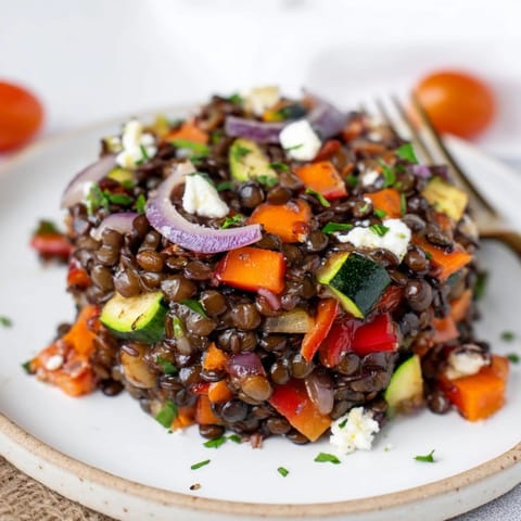 Hearty and healthy, this Black Lentil Salad with Roasted Vegetables showcases colorful veggies and crumbled feta on a rustic plate.