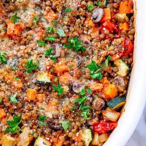 A baked Green Lentil and Vegetable Casserole with golden cheese topping, served in a rustic dish with a fresh parsley garnish.  