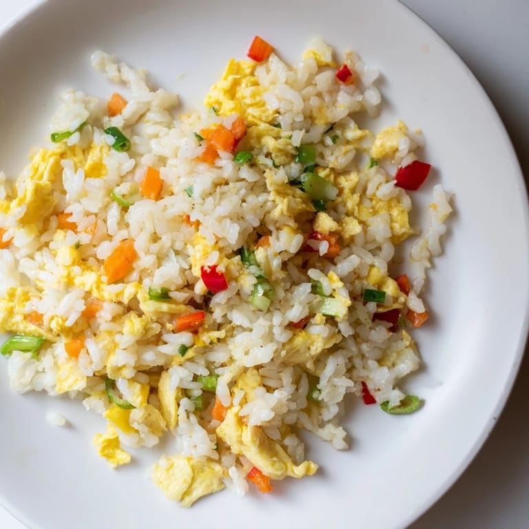 A close-up of golden scrambled eggs mixed into seasoned fried rice with diced red bell pepper and soy sauce aroma.