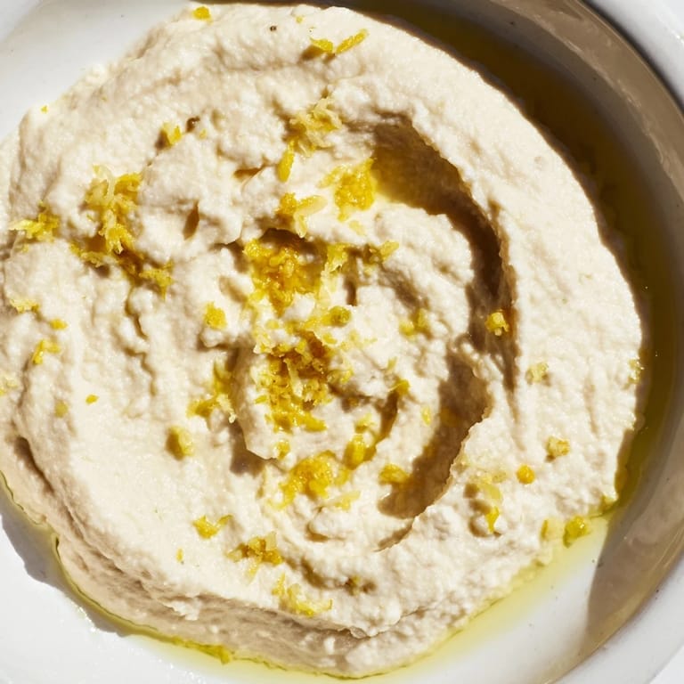 A vibrant White Bean Dip topped with herbs and lemon zest, surrounded by colorful veggie sticks for dipping.  