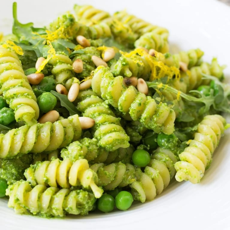 Spring Green Pesto Pasta Salad garnished with lemon zest and pine nuts on a picnic table.