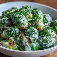 Roasted Brussels sprouts glisten in a rich, creamy Dijon mustard sauce, garnished with fresh parsley for a savory vegetarian dinner side.